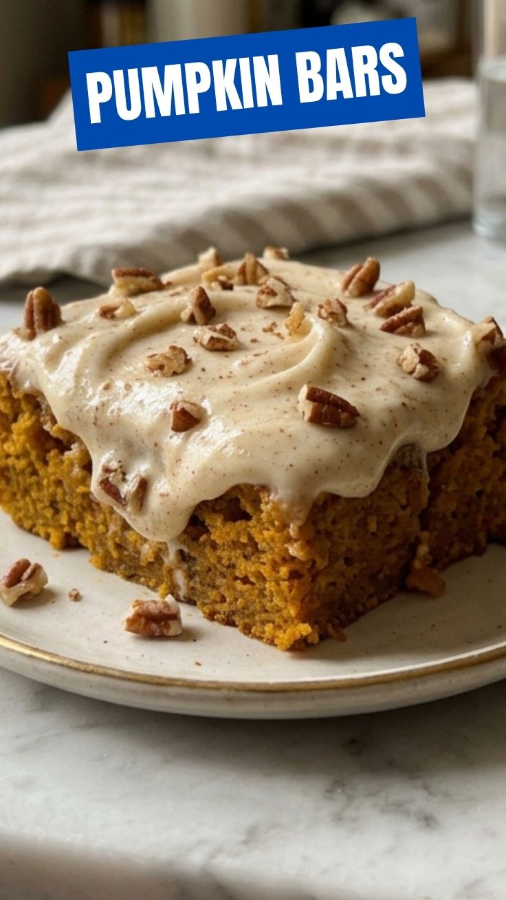 Moist pumpkin bars with cream cheese frosting on a rustic wooden table